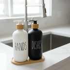 Two soap dispensers, one labeled 'HANDS' and the other 'DISHES', on a wooden stand with a white background.